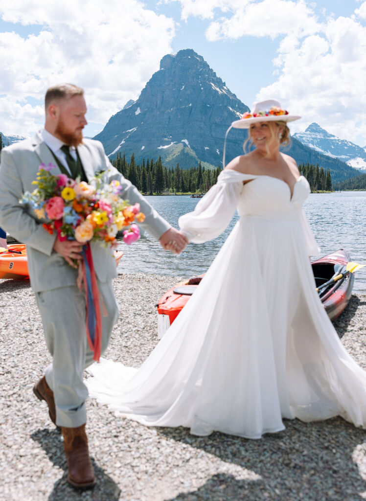 Bride and groom standing by a lake, with the bride's dress flowing in the wind. Beautiful Glacier National Park Elopement Locations