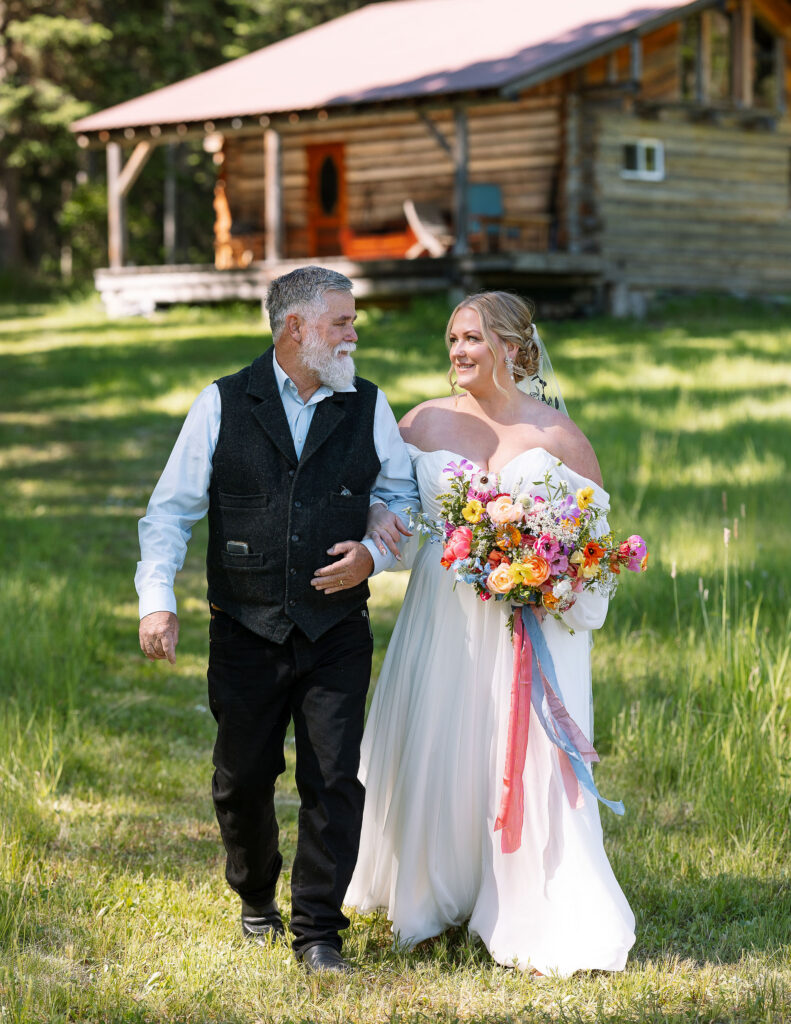 Bride walking with her father towards the ceremony at a scenic outdoor venue.