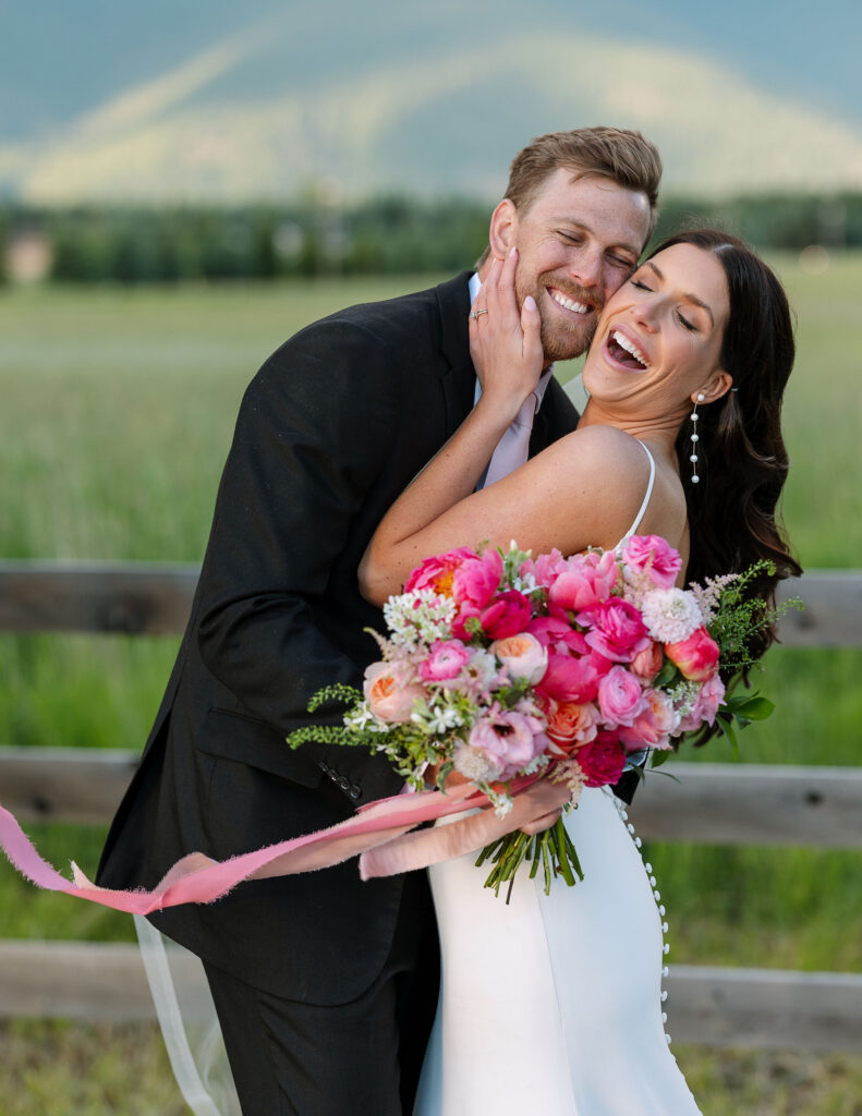 Couple laughing together as the bride holds a bright pink bouquet, capturing candid storytelling photography at a Montana wedding.