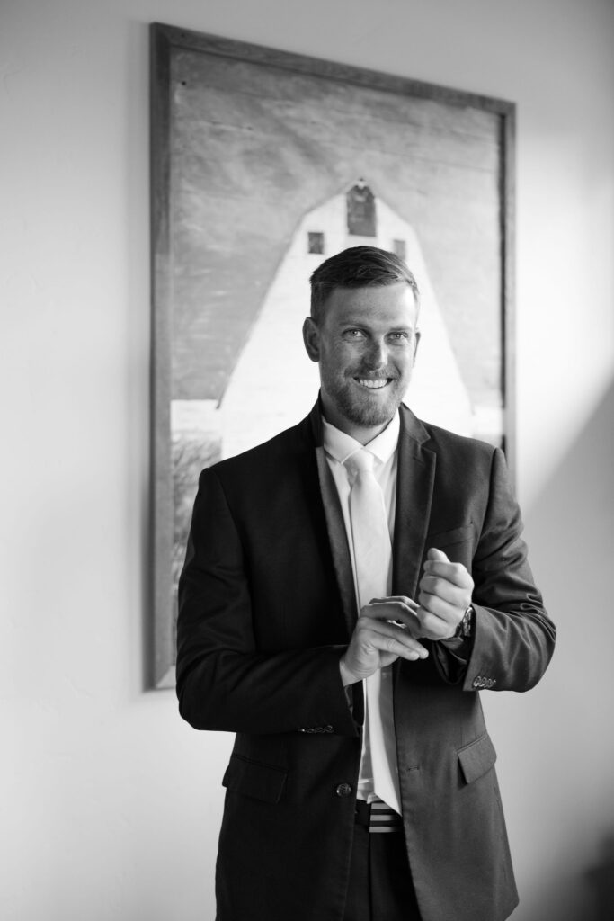 Black-and-white portrait of the groom adjusting his boutonniere, shot by Haley J Photo in Montana.