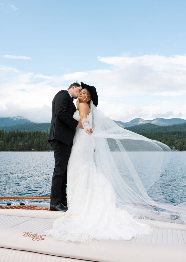 Bride and groom embrace on boat with mountain backdrop in Whitefish Montana