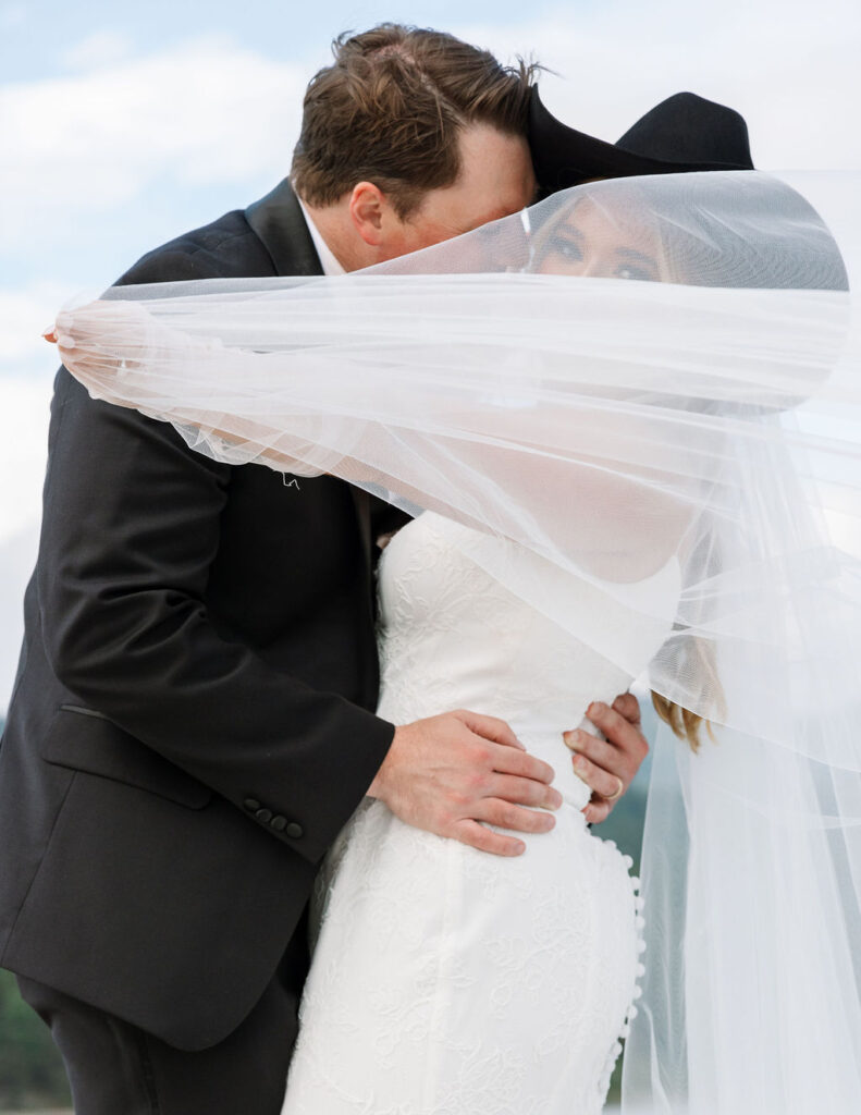 Bride and groom kiss under flowing veil during Whitefish Montana wedding portraits