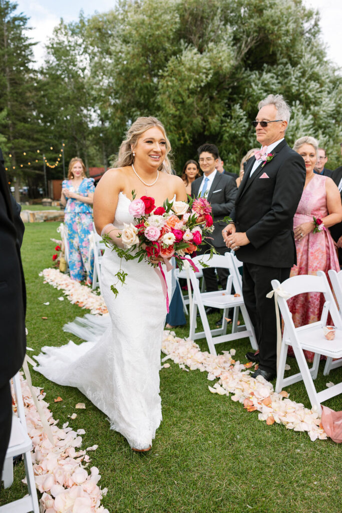 Bride walks down the aisle with vibrant florals at her Whitefish Montana wedding