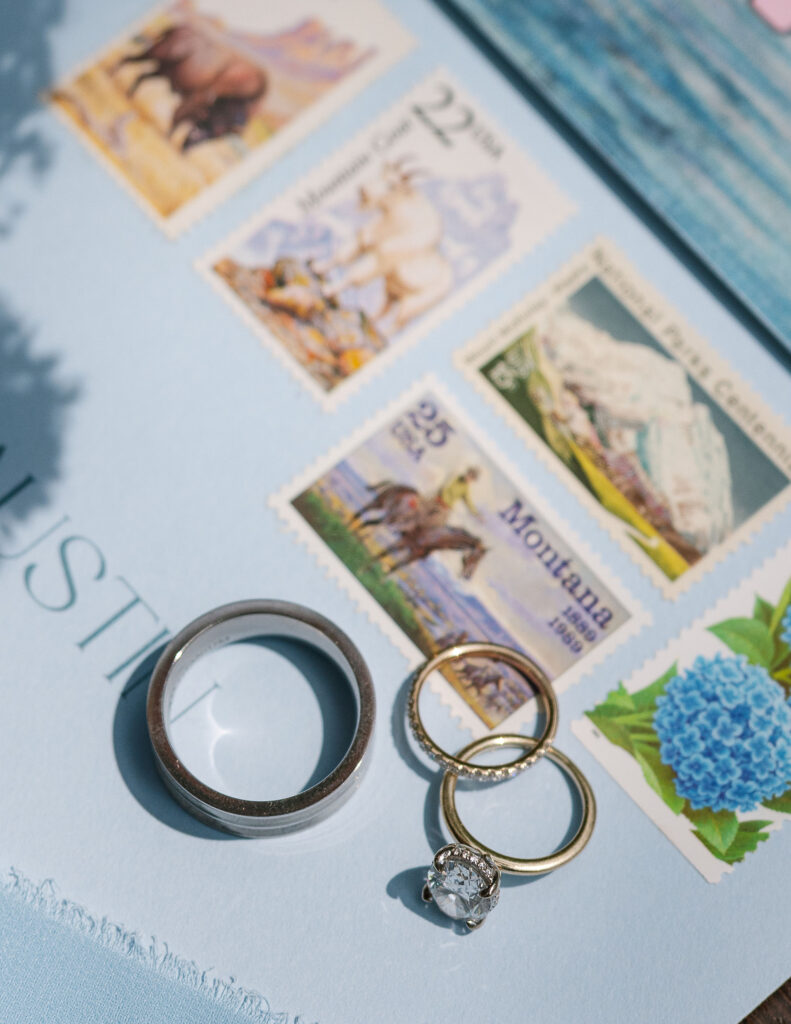 Flat lay of Glacier National Park elopement invitation suite with postcards, mountain artwork, and white flowers.