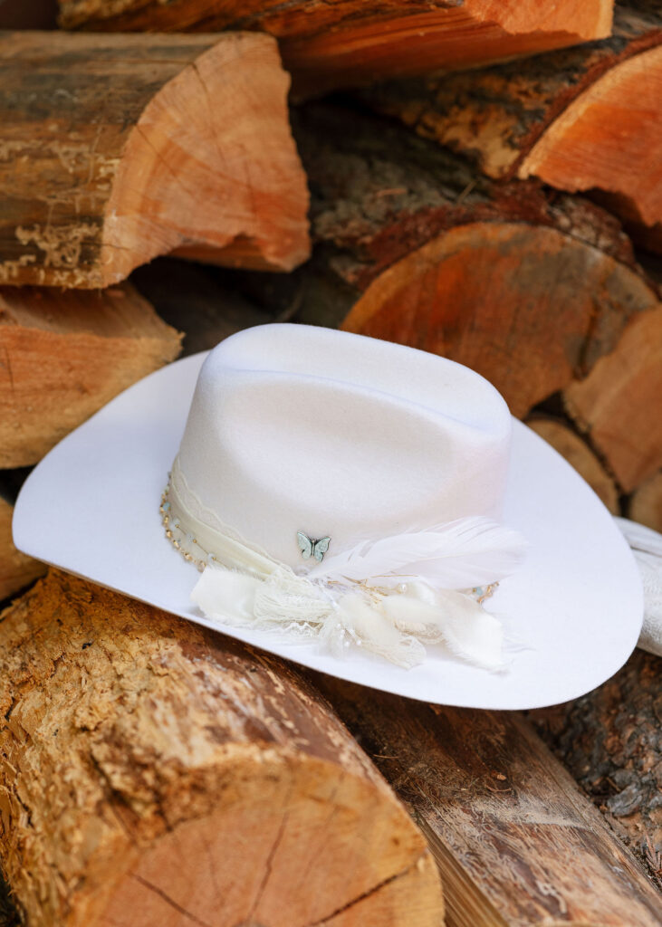 White cowboy hat with feather detail resting on stacked firewood at a Glacier National Park elopement.