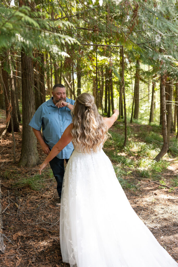 Bride in lace gown walking through the forest to her father for a first look during a Glacier National Park elopement.