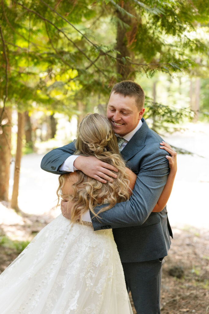 Bride and groom embracing under tall pine trees before their Glacier National Park elopement ceremony.