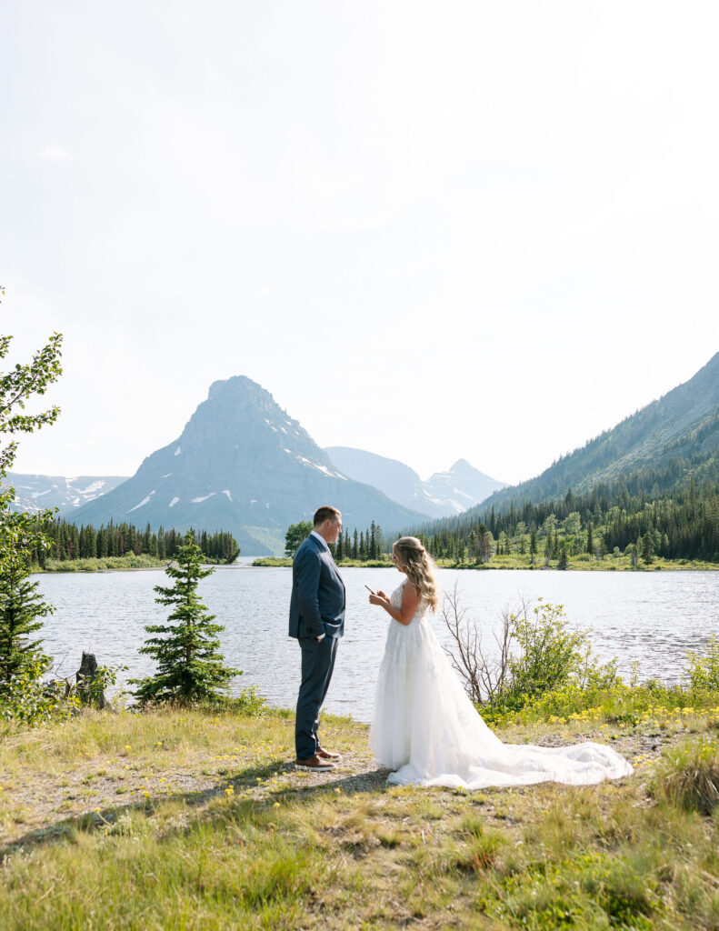 Couple reading vows by the lake with mountains in the background during their Glacier National Park elopement.
