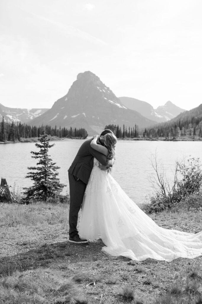 Black and white photo of bride and groom hugging beside a mountain lake at their Glacier National Park elopement.