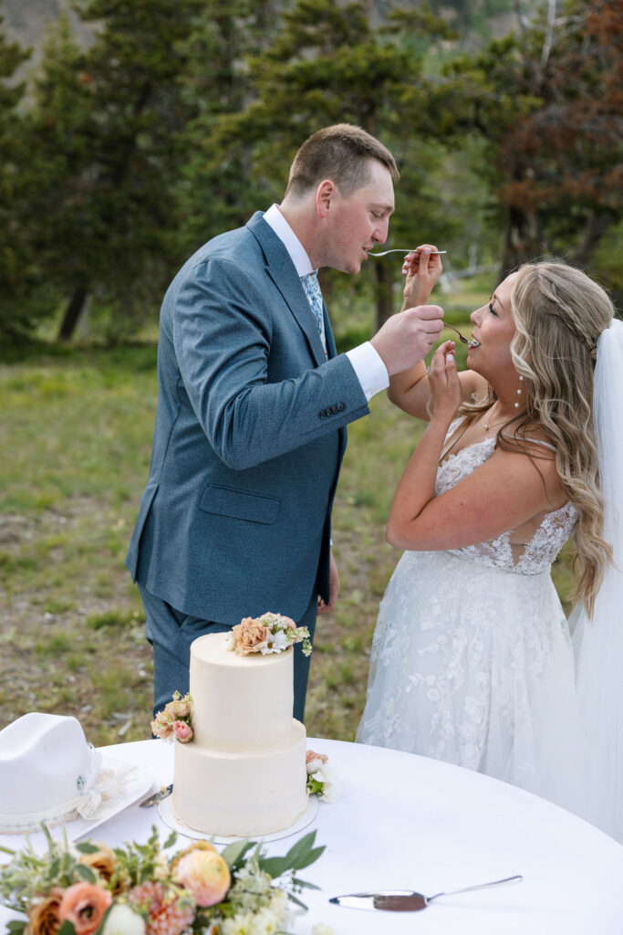 Bride and groom feeding each other wedding cake during their Glacier National Park elopement celebration.