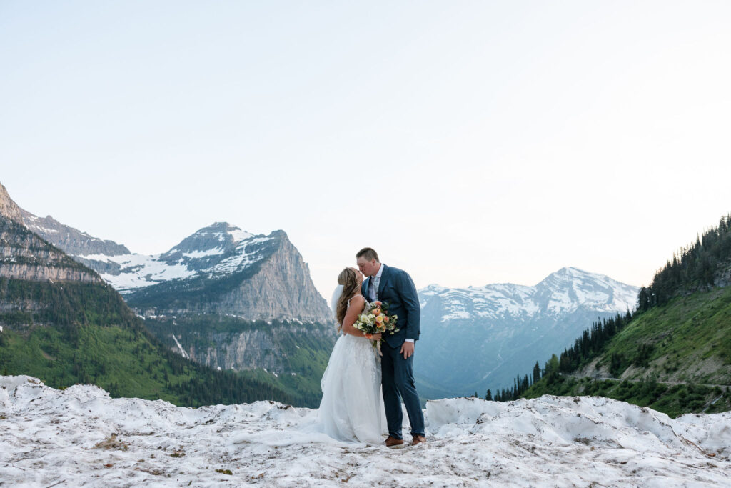 Bride and groom embracing on a snowy overlook with mountain views during their Glacier National Park elopement.