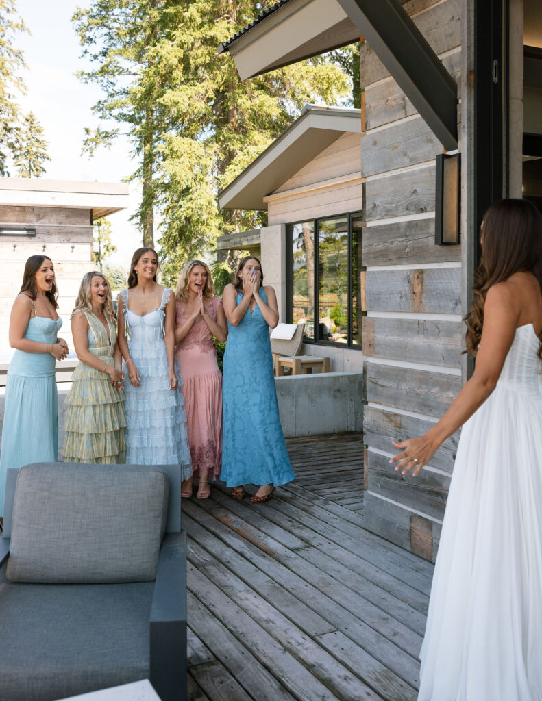 Bridesmaids react with joy and surprise during a first look with the bride on a rustic porch in Kalispell, Montana. Candid, joyful wedding photos.