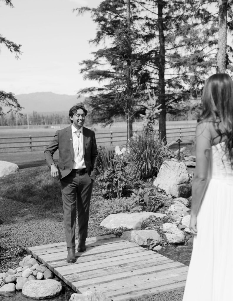 Groom smiles in awe as he sees his bride for the first time during a first look moment at a Montana wedding, surrounded by trees and open fields.