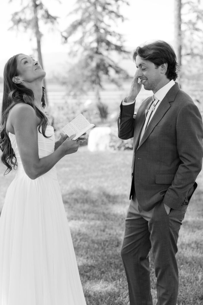 Bride and groom laugh and tear up while reading private vows before their wedding ceremony. Joyful and intimate moment in wedding photos.