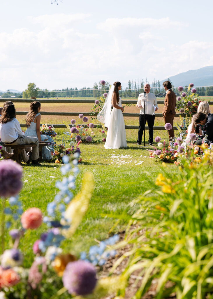 Bride and groom exchange vows in an outdoor ceremony surrounded by wildflower arrangements and mountain views in Whitefish, Montana.