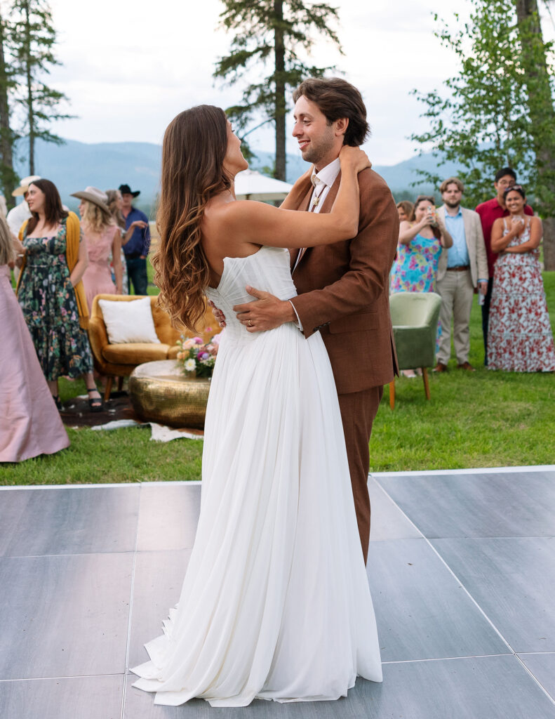 Bride and groom share their first dance surrounded by guests and mountain views at their joyful outdoor Montana wedding reception.