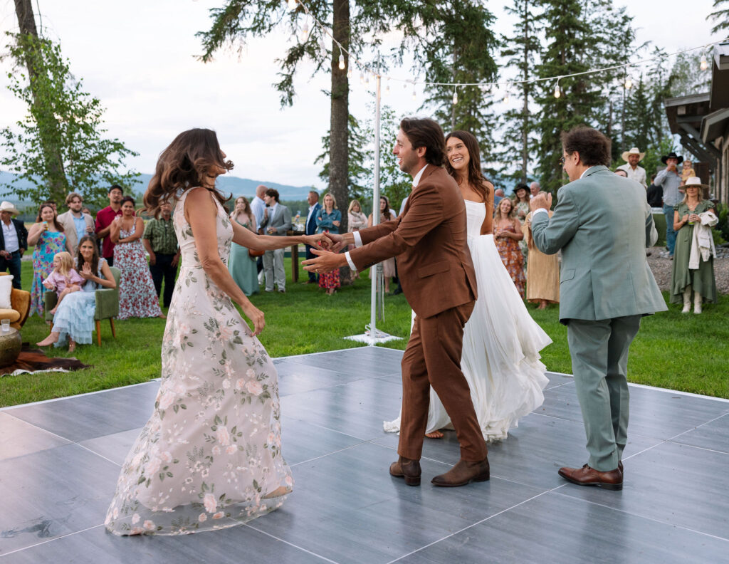 Groom dances with his mother on the outdoor reception dance floor, surrounded by guests and mountain views at a joyful Montana wedding.