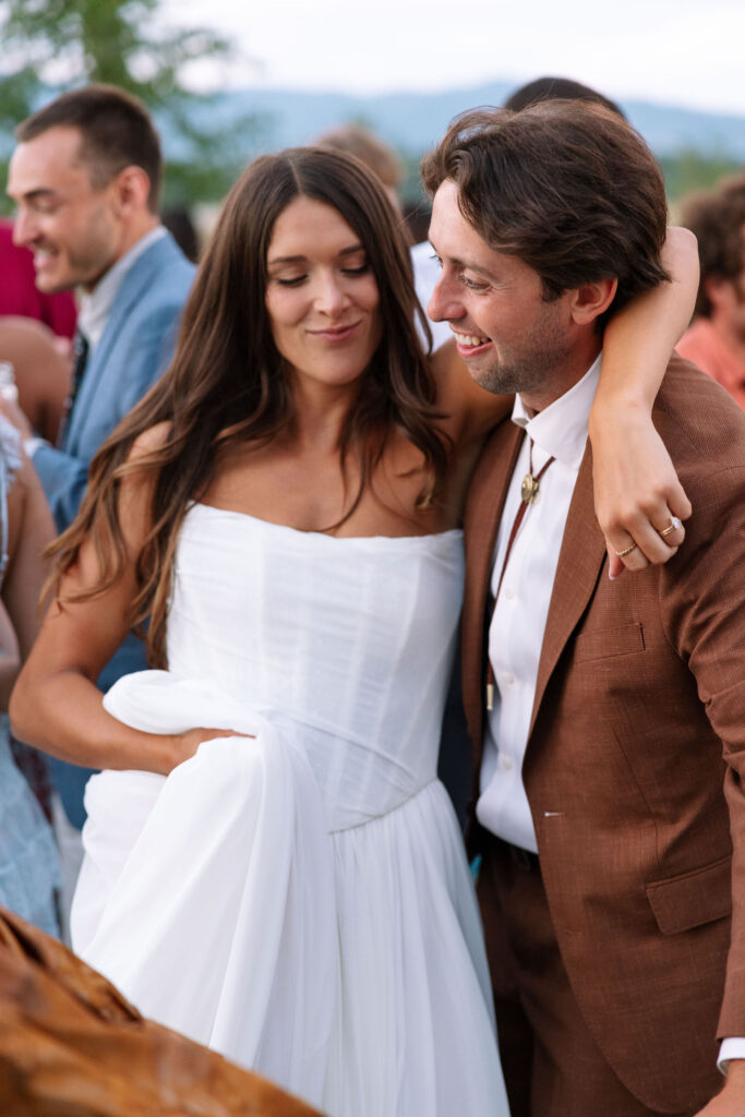 Bride wraps her arm around the groom as they dance together surrounded by friends — candid newlywed joy on the dance floor at their Montana wedding.
