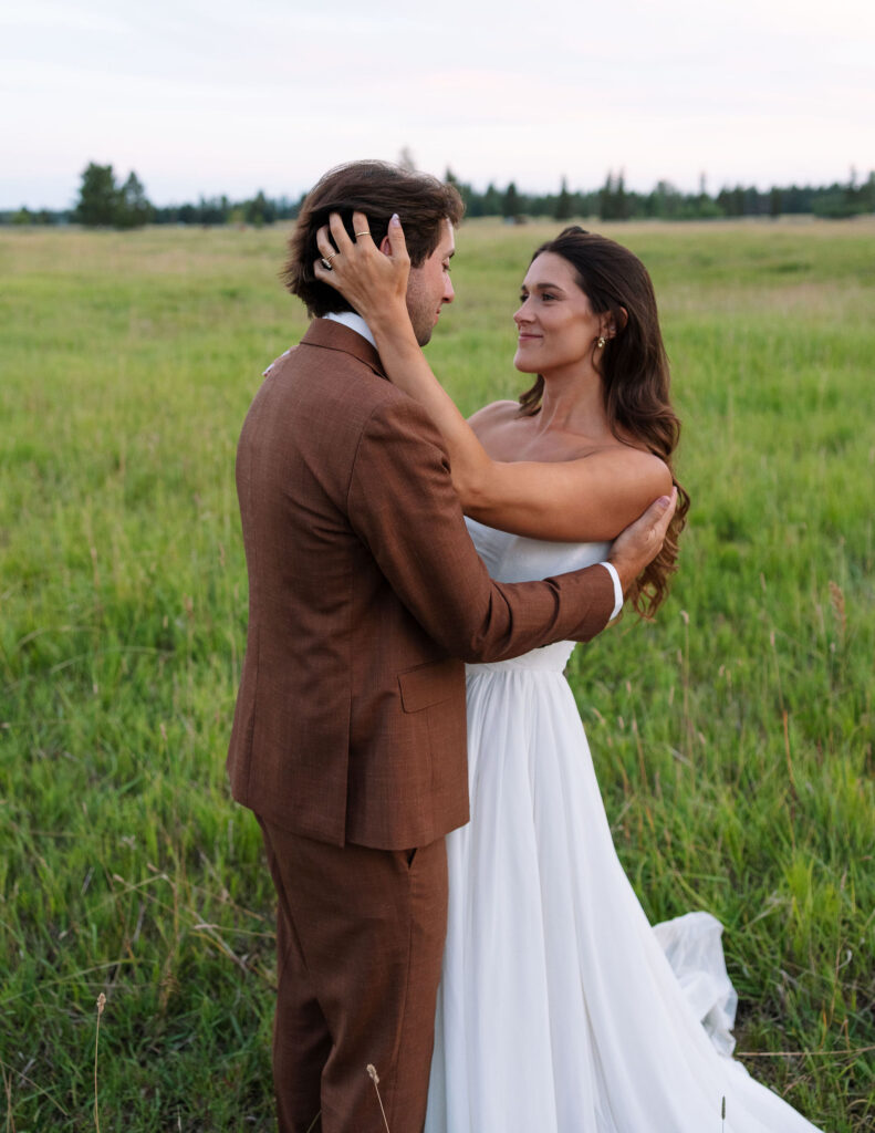 Bride and groom share an intimate gaze in a wild grassy field near Kalispell, Montana, radiating calm, connection, and genuine joy.
