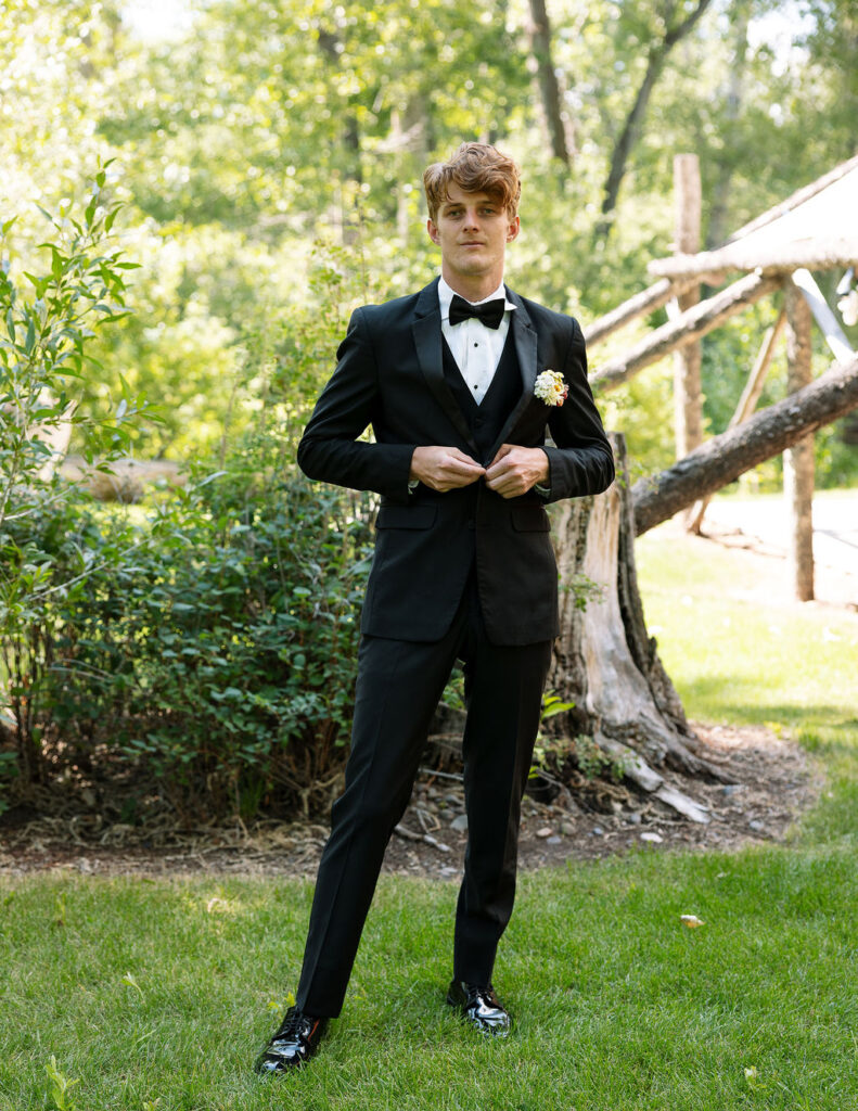 Groom adjusting his tuxedo jacket in the garden at Rockin’ TJ Ranch in Bozeman before the wedding ceremony.