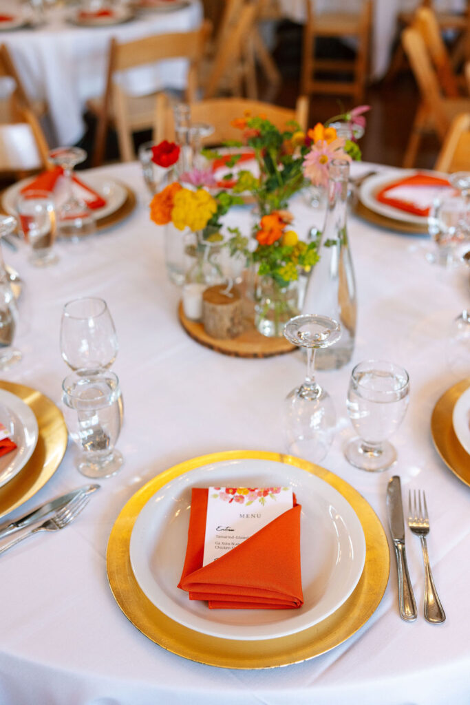 Wedding reception table at Rockin’ TJ Ranch in Bozeman styled with bright floral centerpieces, orange napkins, and elegant glassware.
