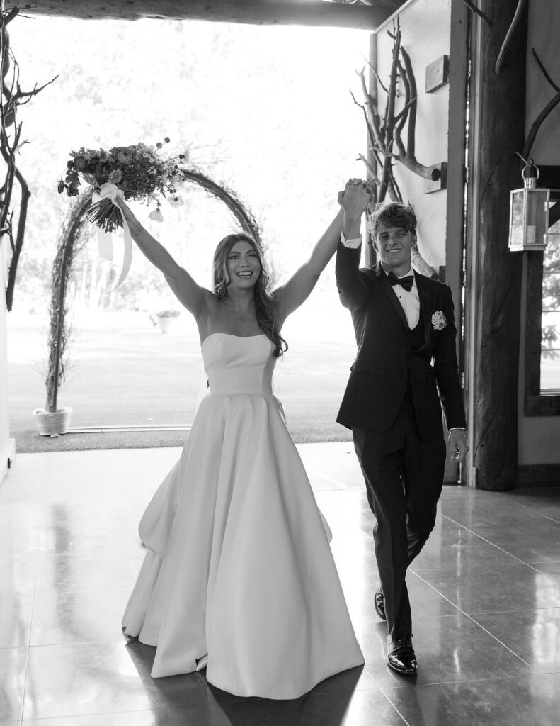 Bride and groom celebrating with raised hands after being announced as newlyweds inside Rockin’ TJ Ranch’s reception space in Bozeman.