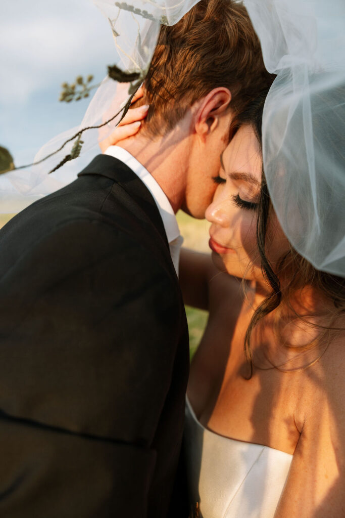 Bride and groom sharing a quiet, romantic moment forehead to forehead with the bride’s veil gently wrapping them together at Rockin’ TJ Ranch.