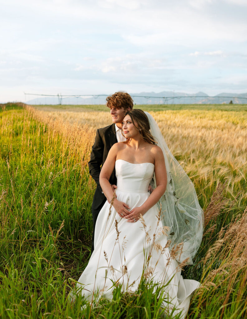 Bride and groom standing closely together in a Montana field at Rockin’ TJ Ranch, framed by tall grass and glowing sunset light.