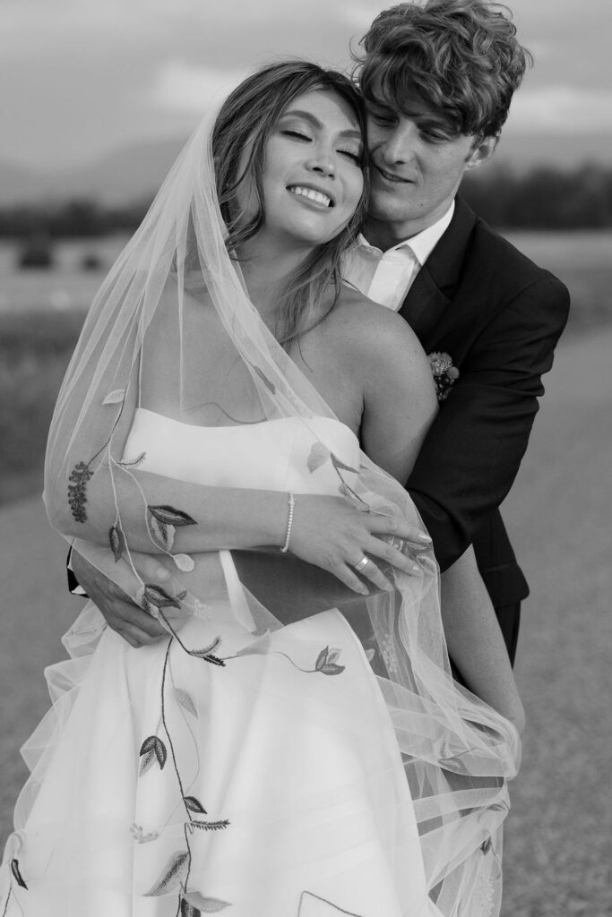 Bride and groom embrace during their Rockin’ TJ Ranch wedding in Bozeman, Montana, smiling joyfully as her veil flows around them.