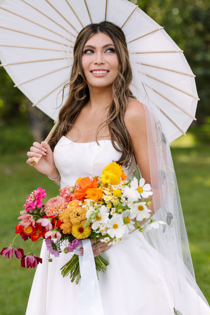 Bride holding a vibrant summer bouquet of orange, yellow, and white flowers during her Rockin’ TJ Ranch wedding in Montana.