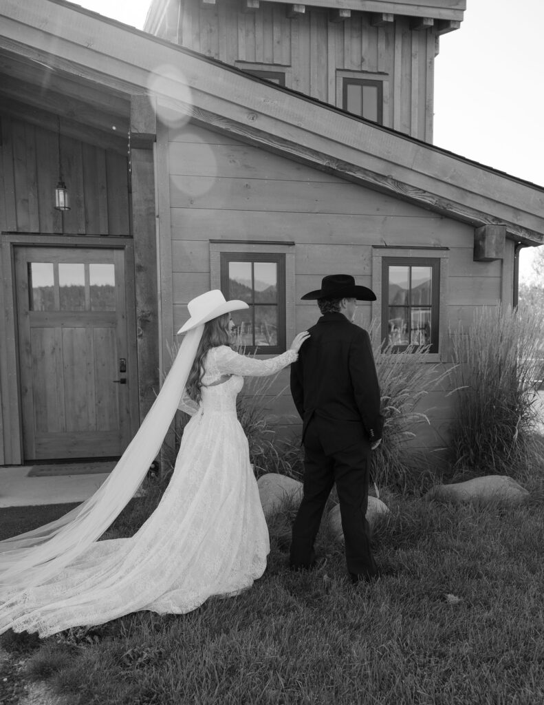 Bride and groom standing outside their cabin at Clydesdale Outpost, her long veil flowing in the breeze during their Montana elopement.