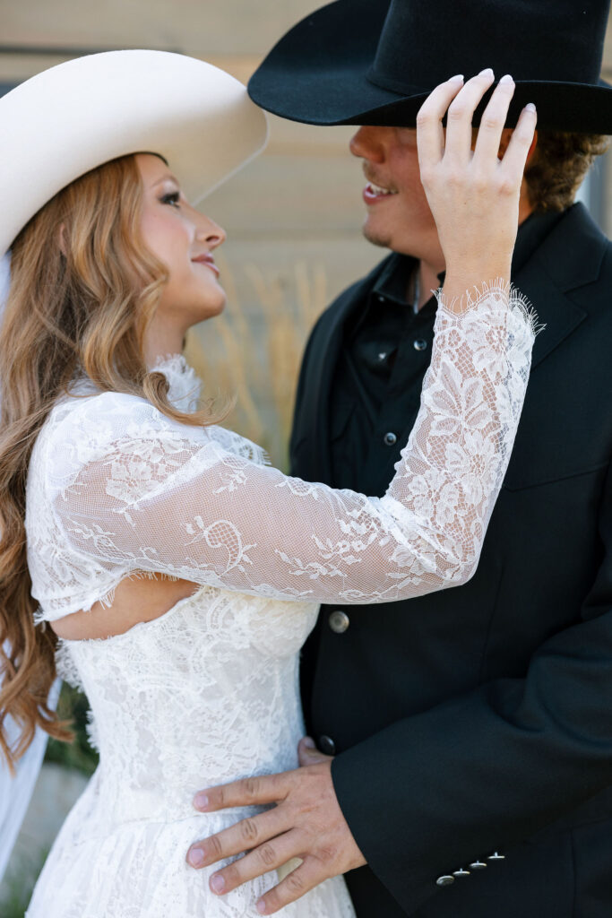 Bride smiling up at her groom while adjusting his cowboy hat during their Montana elopement at Clydesdale Outpost.