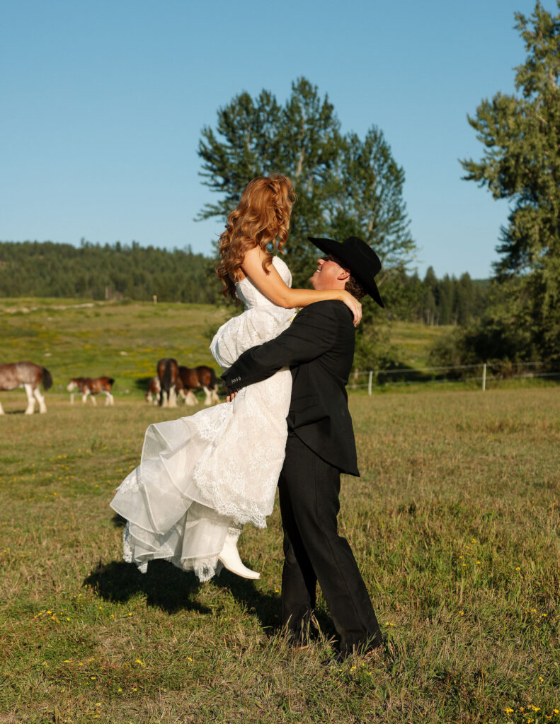 Bride and groom standing in a vast Montana pasture with Clydesdale horses nearby, embodying a true Western elopement at Clydesdale Outpost.