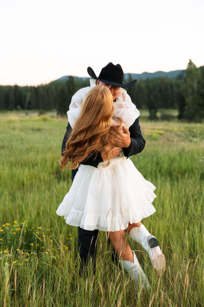 Groom lifting the bride in a grassy Montana field surrounded by mountain views during their Clydesdale Outpost elopement.