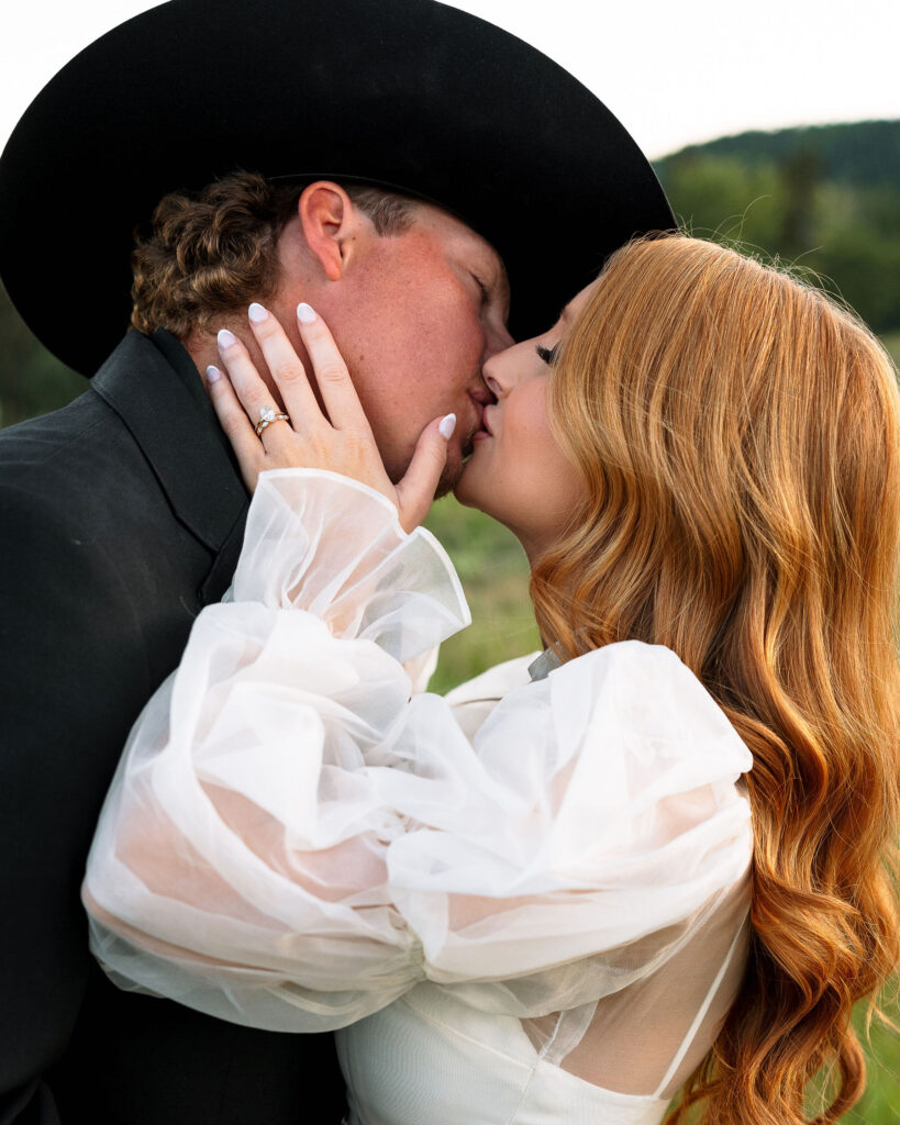 Bride and groom sharing a kiss during their Montana elopement at Clydesdale Outpost, captured in golden light with Western-inspired attire.