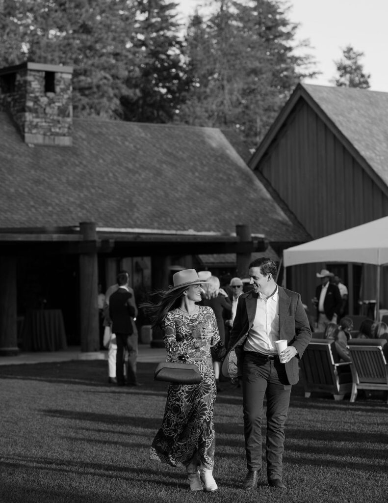 Black and white candid of guests mingling outside the rustic lodge at Iron Horse during Mary and Zack’s Whitefish rehearsal dinner