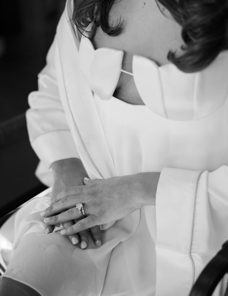 Close-up of the bride’s hands and wedding ring as she adjusts her gown