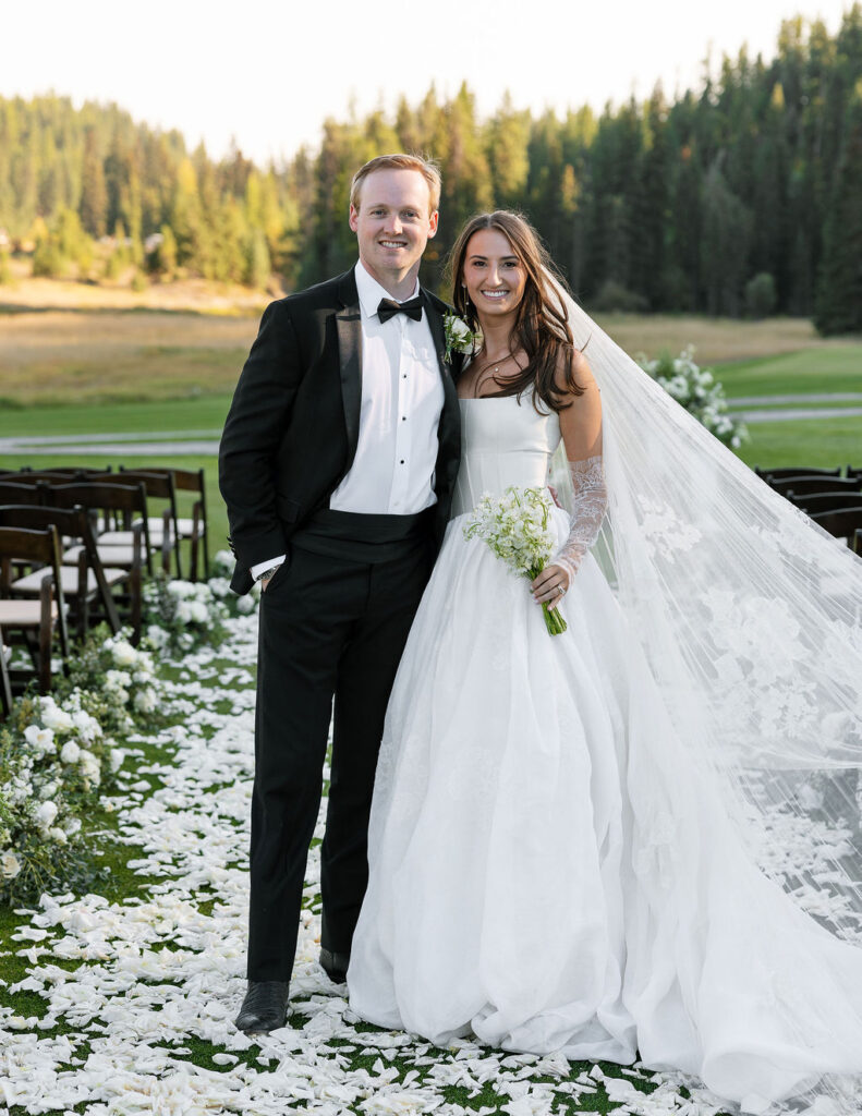 Bride and groom standing together on the ceremony lawn with white florals around them