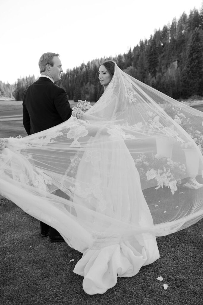 Groom looking at the bride as her veil blows in the wind during portraits