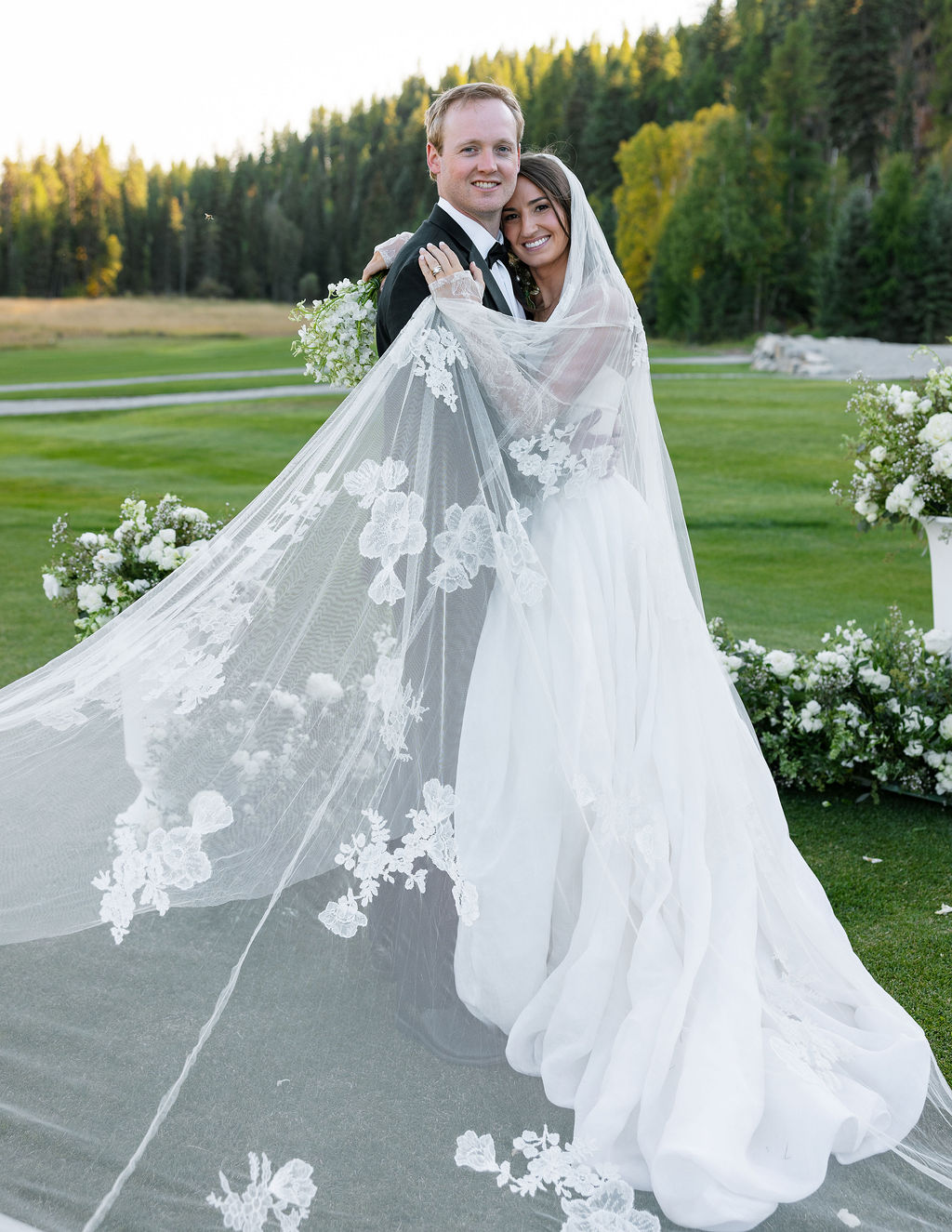 Bride and groom walking across the golf course with the bride’s veil flowing