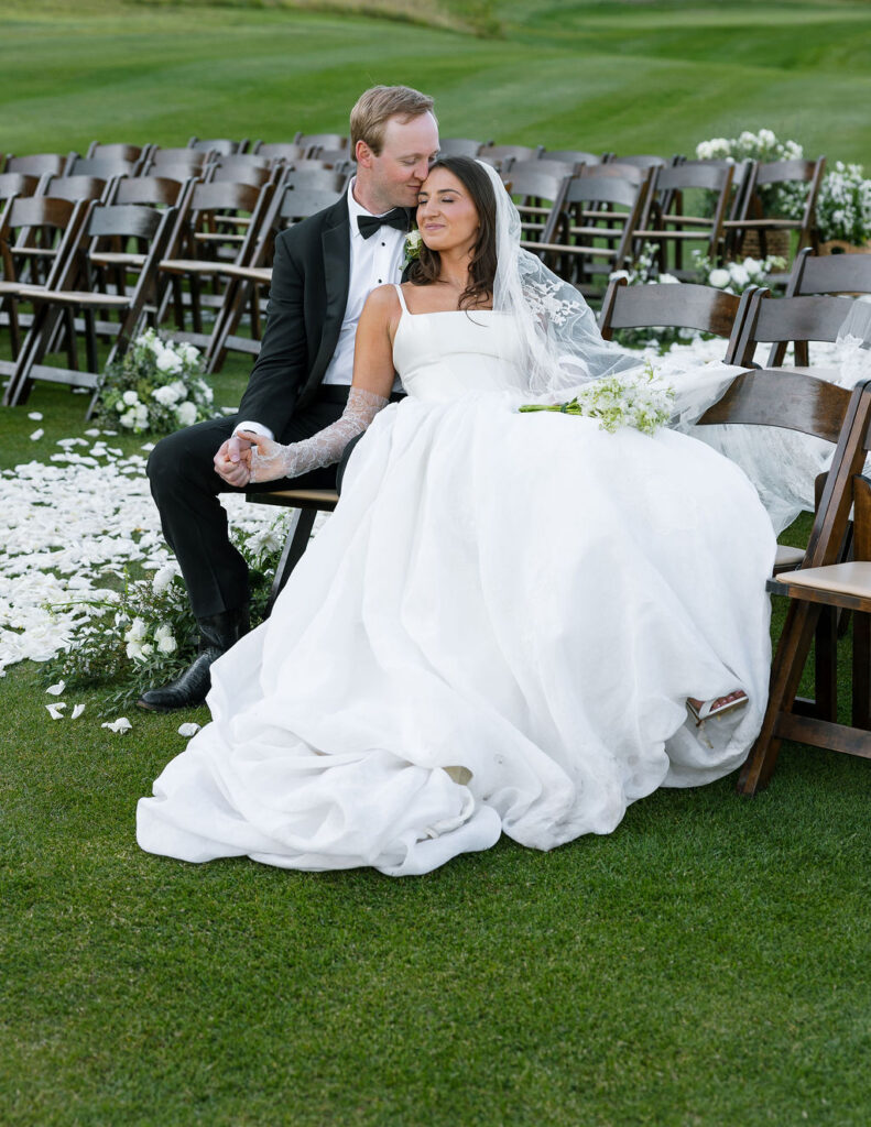 Bride and groom sitting together during their ceremony surrounded by floral aisle decor
