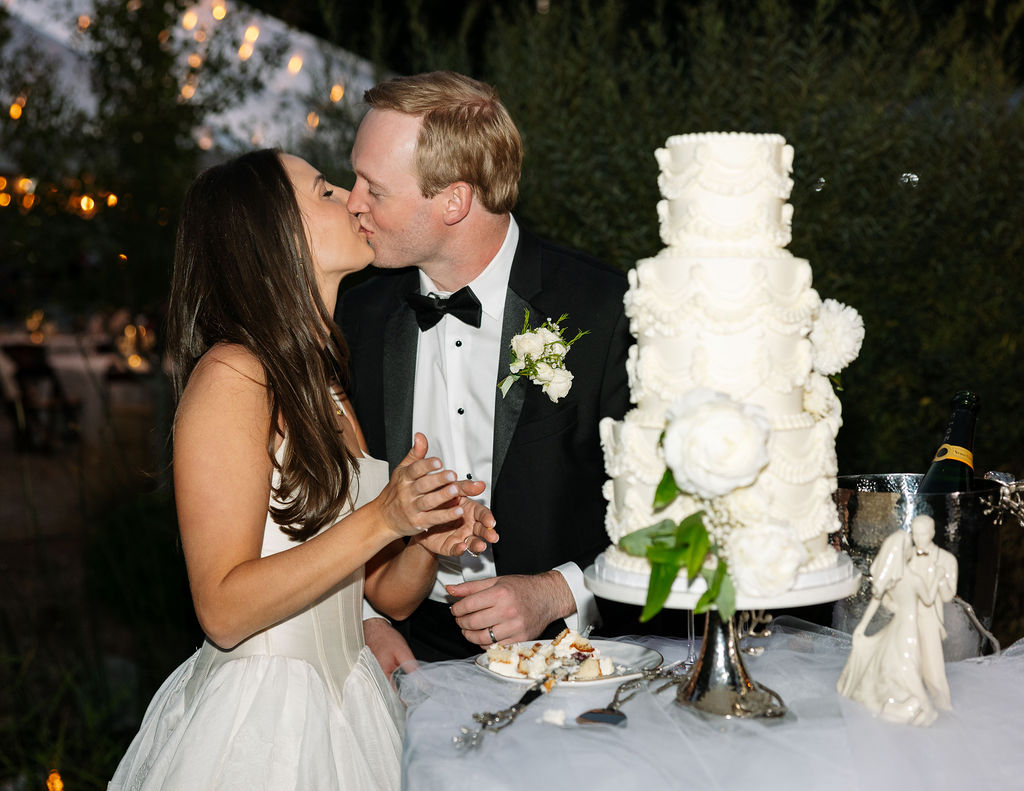 Bride and groom kissing beside a tall white floral wedding cake