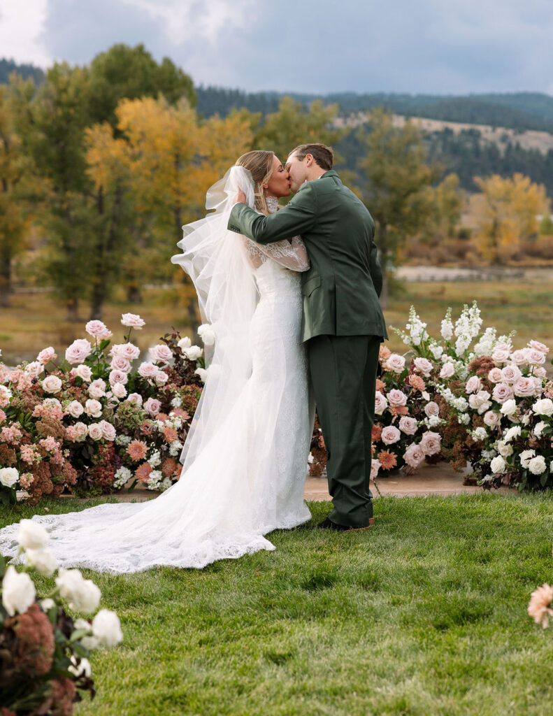 Bride and groom embracing at floral ceremony backdrop during Montana ranch wedding