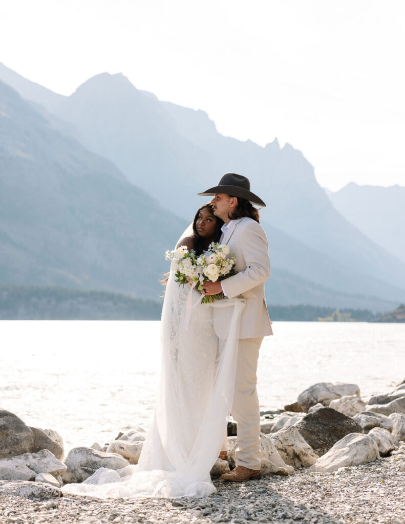 Bride and groom hugging beside alpine lake during fall elopement in Glacier National Park
