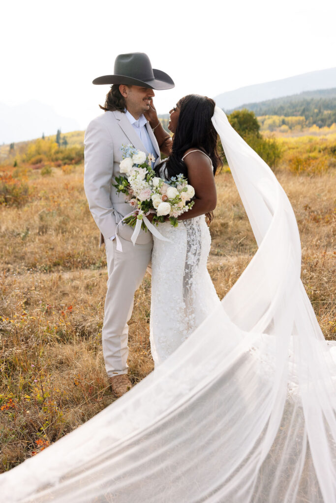 Bride and groom embracing in fall landscape with veil flowing during Glacier National Park elopement