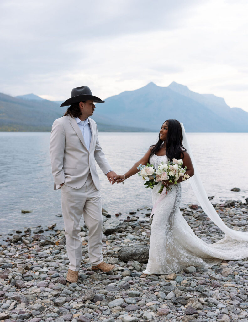 Bride and groom holding hands beside alpine lake during fall elopement in Glacier National Park
