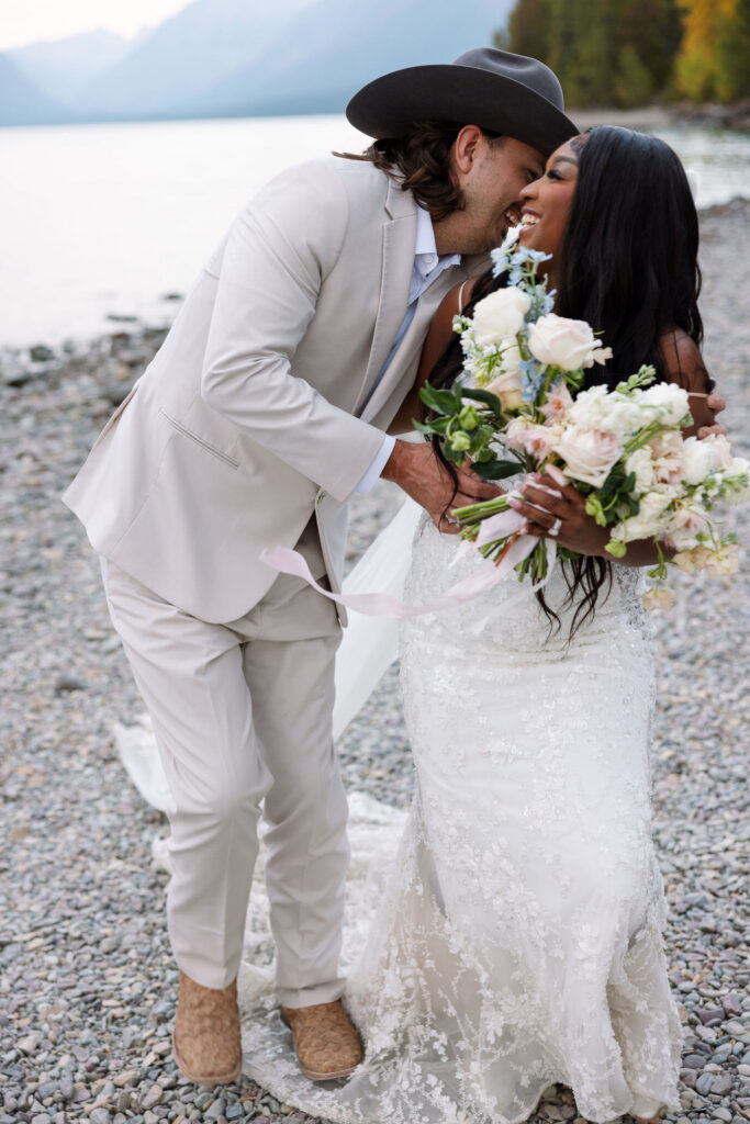 Groom kissing bride on the forehead while holding bouquet during fall elopement in Glacier National Park