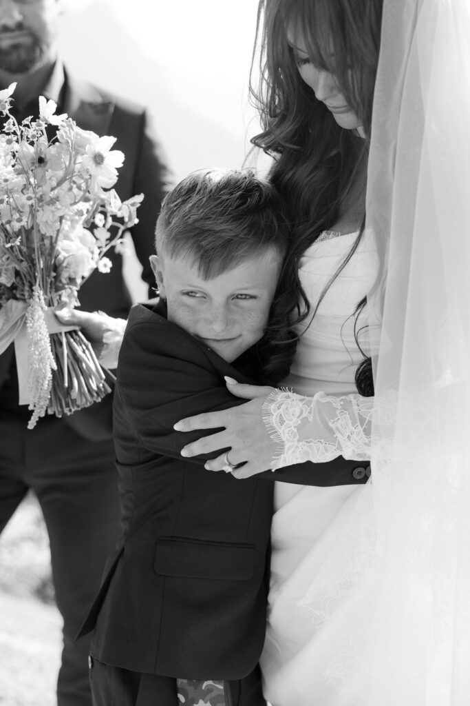 Black and white close portrait of bride hugging a young boy during a Glacier National Park elopement
