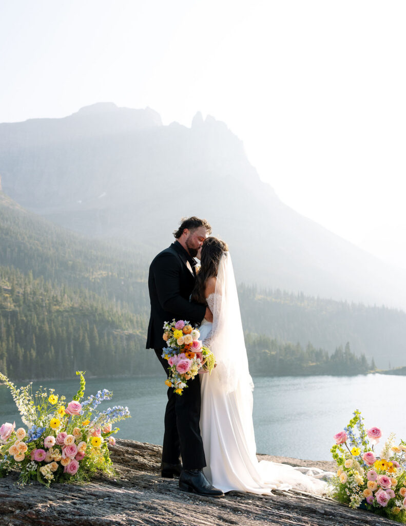 Bride and groom embracing beside a glacial lake during a Glacier National Park elopement ceremony