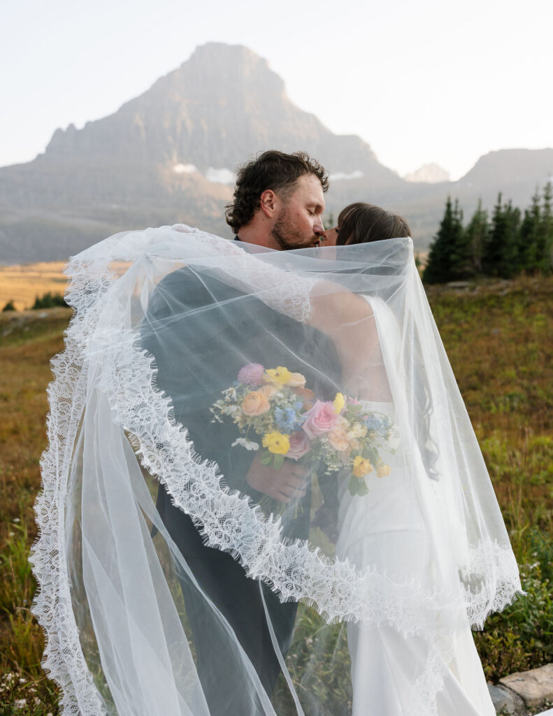 Bride and groom wrapped in the bride’s veil with colorful bouquet during a Glacier National Park elopement